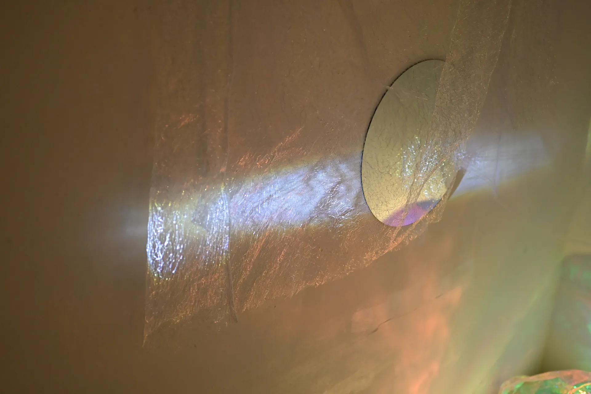 Colored light crosses sheer fabric beside a suspended circular mirror