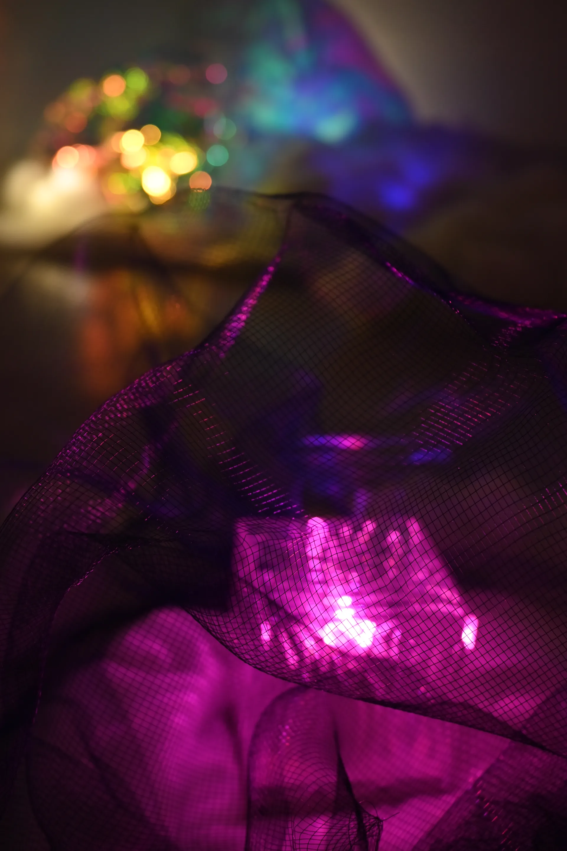 A violet glow shines through layers of dark mesh with distant colored reflections