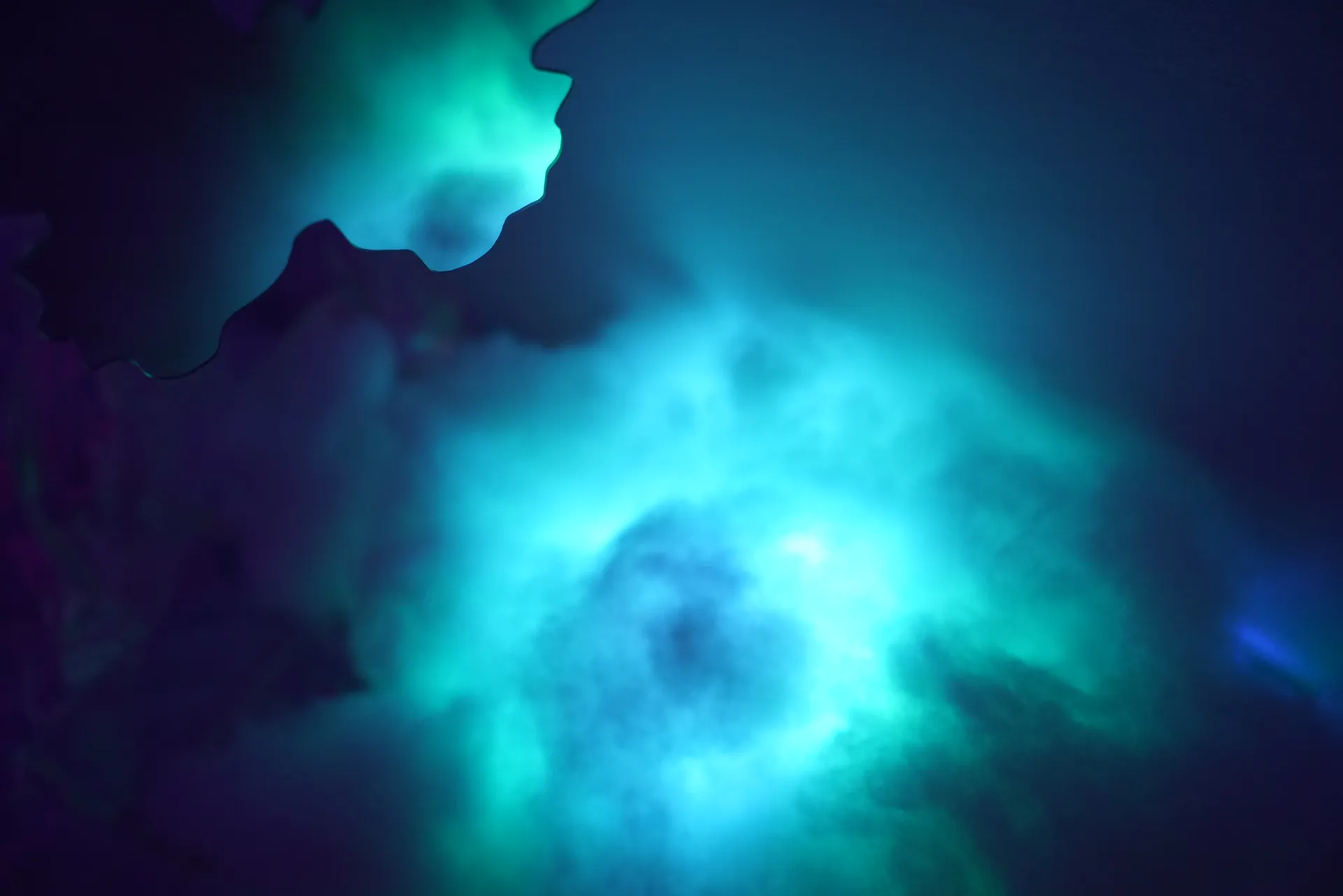 Turquoise light blooms through cloudlike fibers beside a reflective edge