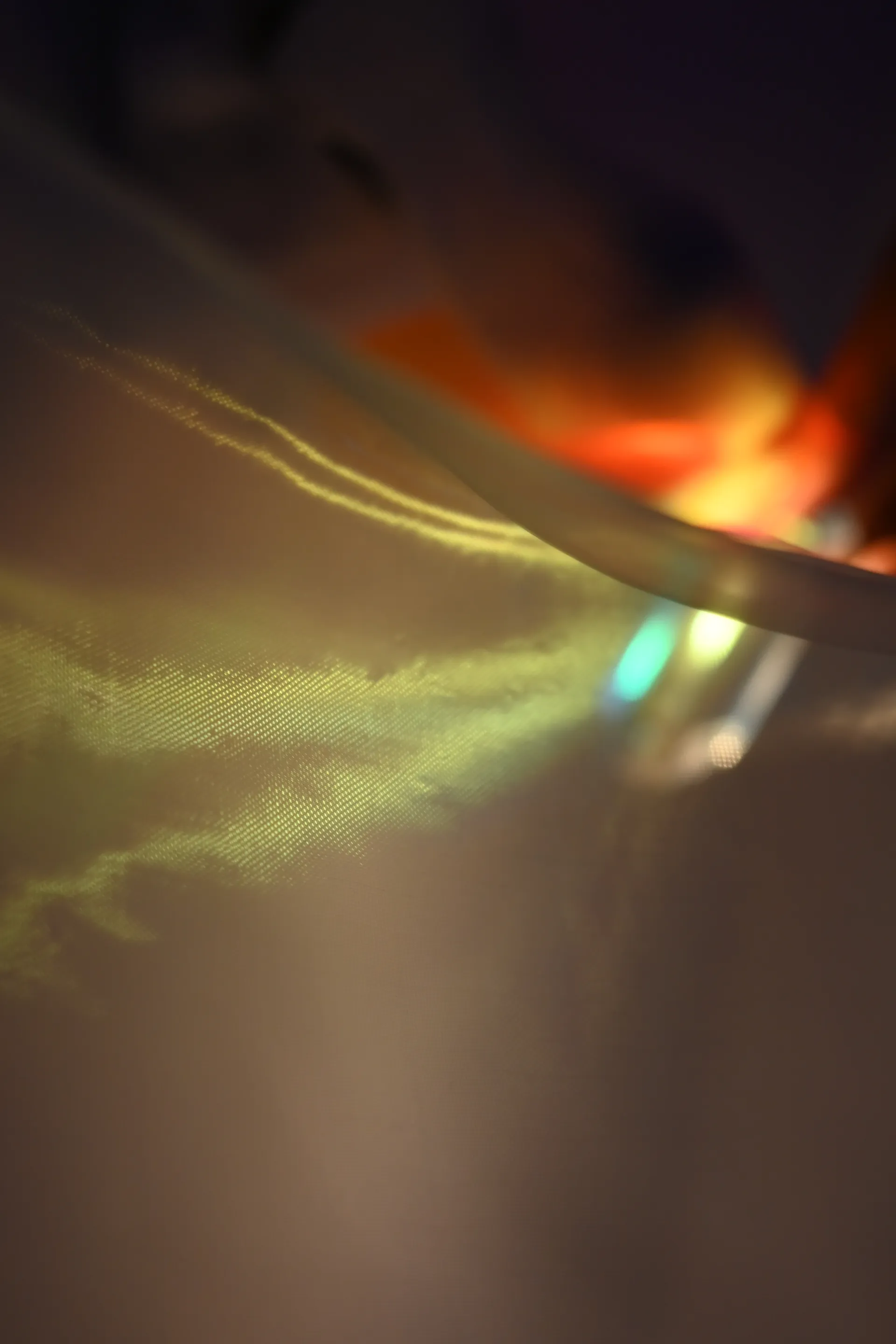 Yellow and green light streaks across sheer fabric beneath a blurred warm reflection